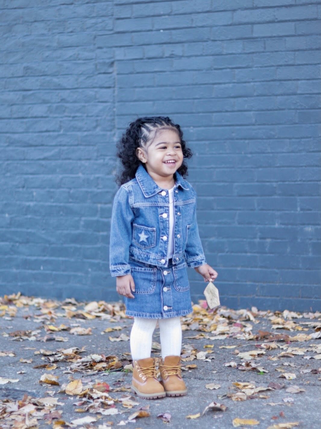 Twin girl smiling in a denim set against a blue brick wall