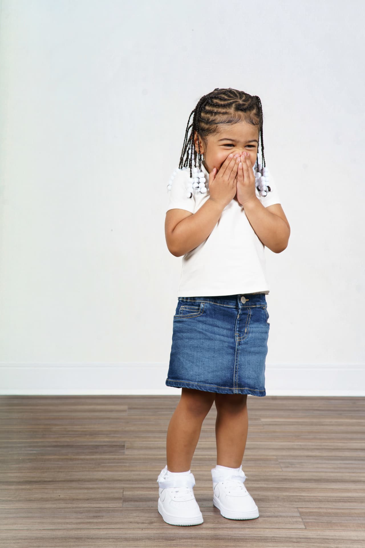 Twin girl in a white top and denim skirt covering her mouth as she giggles