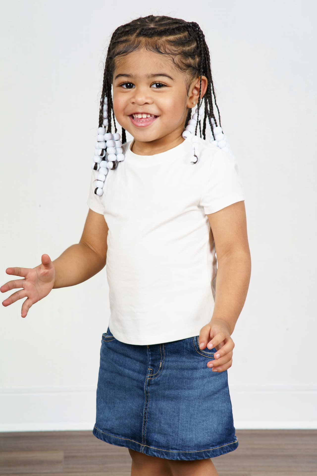 Twin girl in a white tee and denim skirt reaching out and smiling