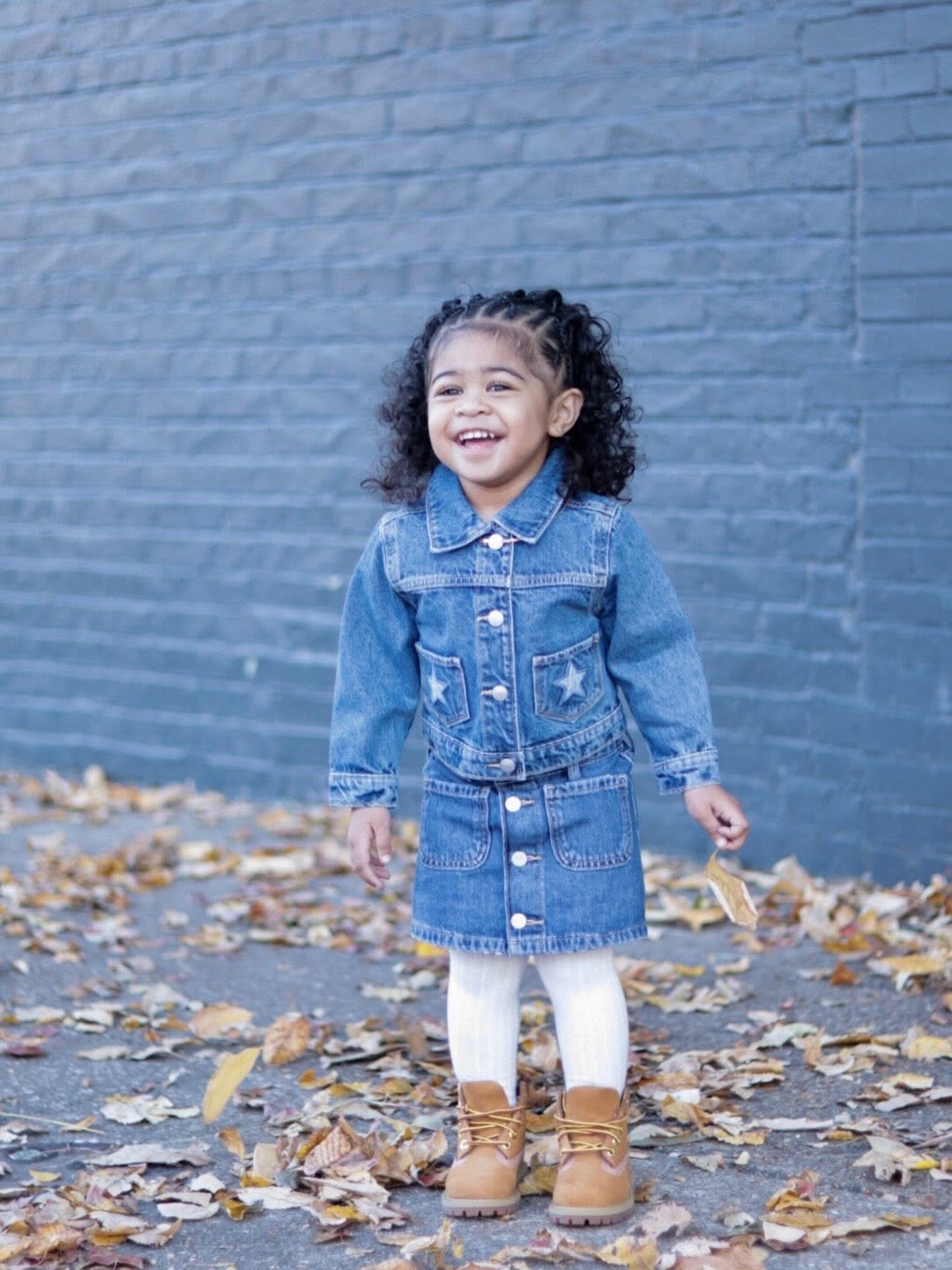 Twin girl laughing in a denim jacket among autumn leaves