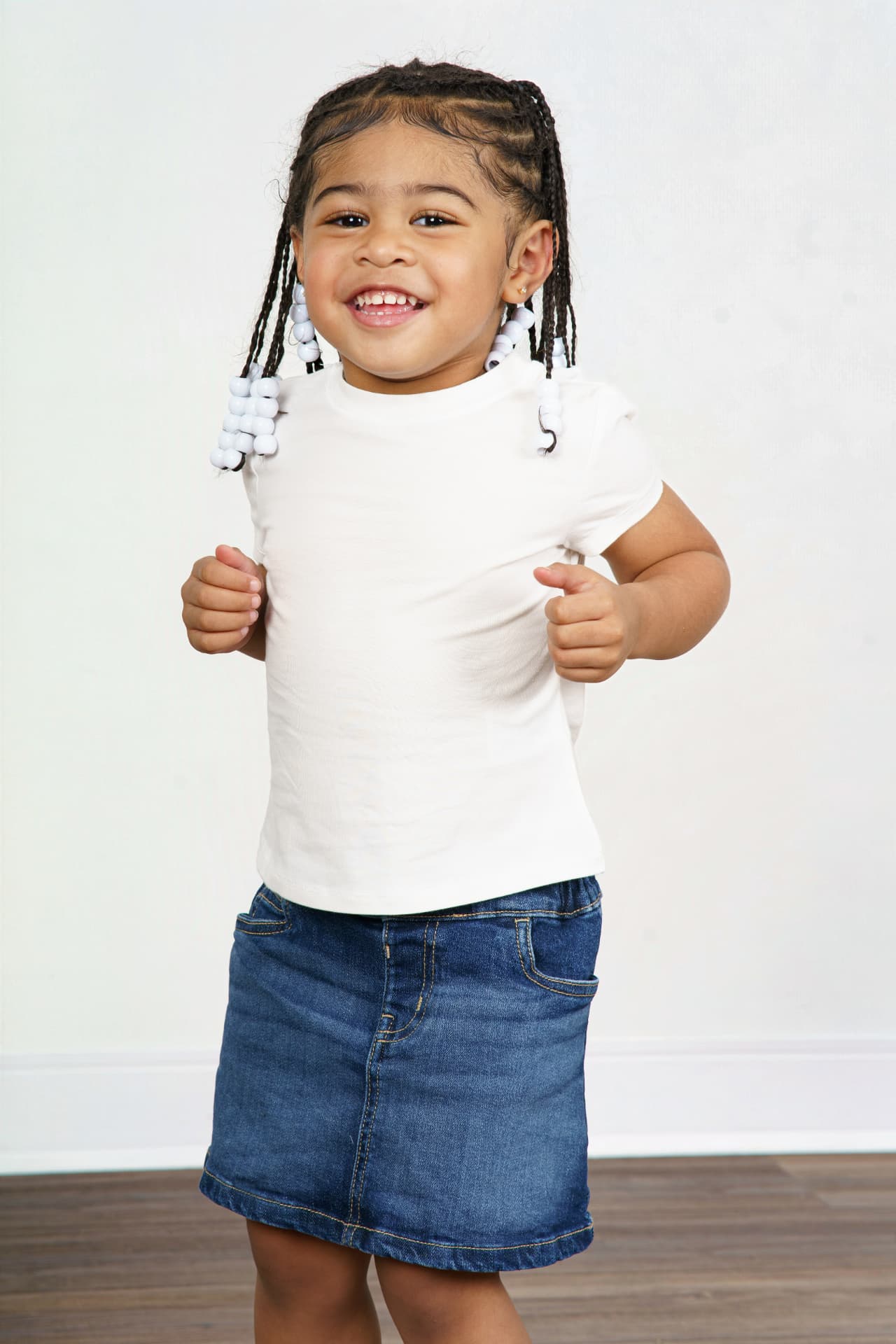 Twin girl in a white tee and denim skirt smiling with fists up